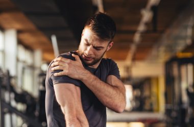handsome young man feeling the pain in shoulder at the gym