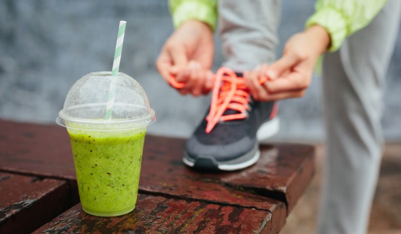 Green detox smoothie cup and woman lacing running shoes before workout