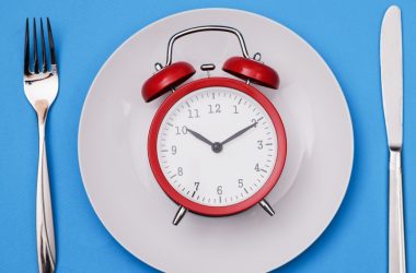 Red alarm clock lies on plate next to fork and knife